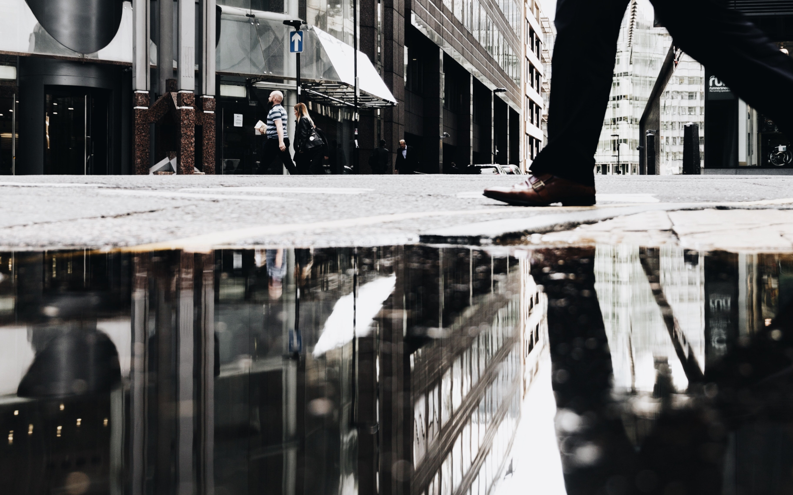 Monochrome photo of a man walking with his reflection in a water pond in the street